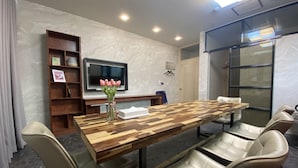 A conference room with a wooden table, beige chairs, a TV on the wall, and a vase with flowers. - Hotel Dm (Seoul)