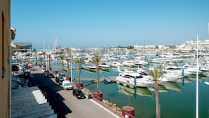 A marina with numerous boats docked, a clear sky, and a road with parked cars. - Marina Pearl - Vilamoura (Vilamoura)