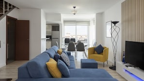 A modern living room with a sofa, chairs, a TV, and a dining area in the background. - Marina Pearl - Vilamoura (Vilamoura)