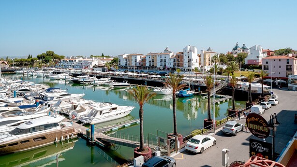 A marina with boats docked, a restaurant sign, and buildings in the background. - Marina Pearl - Vilamoura (Vilamoura)