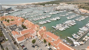 A marina with numerous boats docked, surrounded by residential buildings with red-tiled roofs. - Marina Pearl - Vilamoura (Vilamoura)