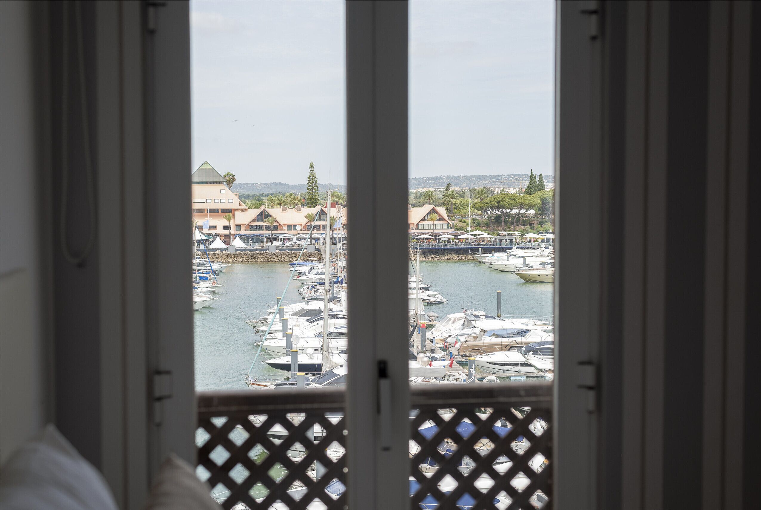Vista desde una ventana sobre un puerto deportivo con barcos amarrados, un edificio con techo característico y un paisaje distante.