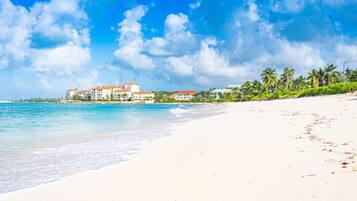 A beach with a clear sky, a sandy shore, and buildings with red roofs in the background.