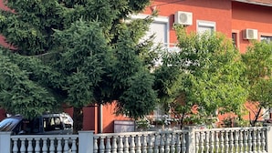 A red building with a tiled roof, surrounded by a white fence and greenery.