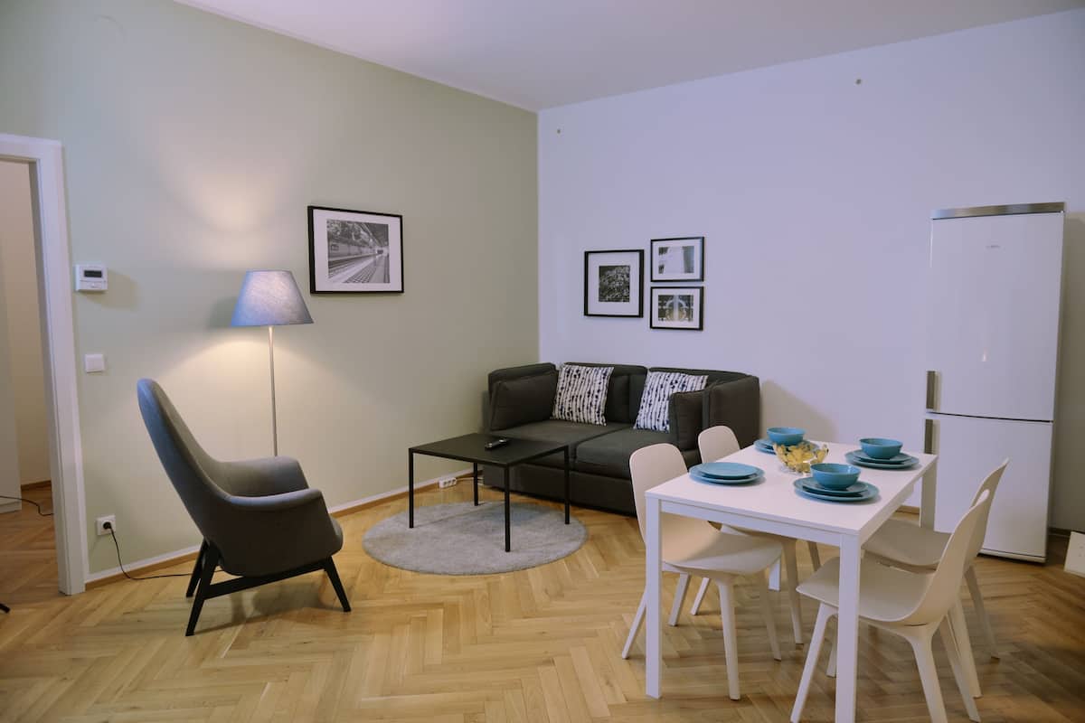 A modern living room with a sofa, a dining table with chairs, a lamp, and framed pictures on the wall.