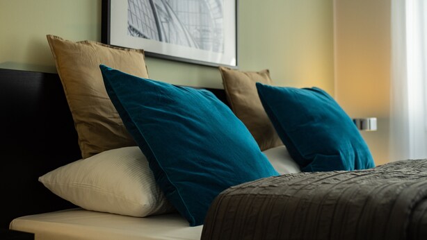 A bed with a headboard, multiple pillows, and a framed picture on the wall. - Jimmy's Apartments Suites (Vienna)