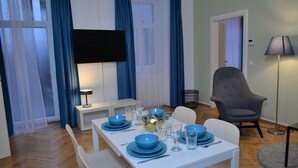 A dining area with a white table set for four, blue tableware, and a grey armchair. - Jimmy's Apartments Suites (Vienna)