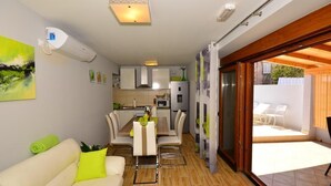 Un espace de vie compact comprenant un coin repas, une kitchenette et une porte-fenêtre coulissante donnant sur une terrasse extérieure.