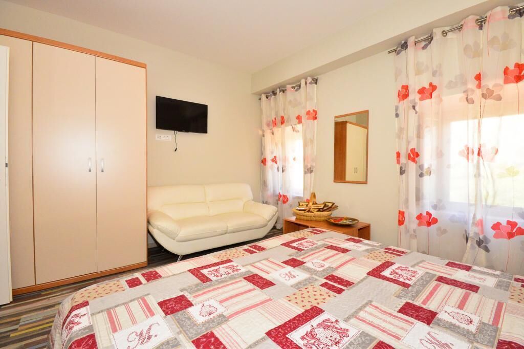 A bedroom with a bed, a sofa, a wardrobe, a television, and a window with curtains.