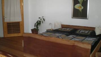 A bedroom with a wooden bed, a potted plant, a wall-mounted lamp, and a framed picture of a flower.
