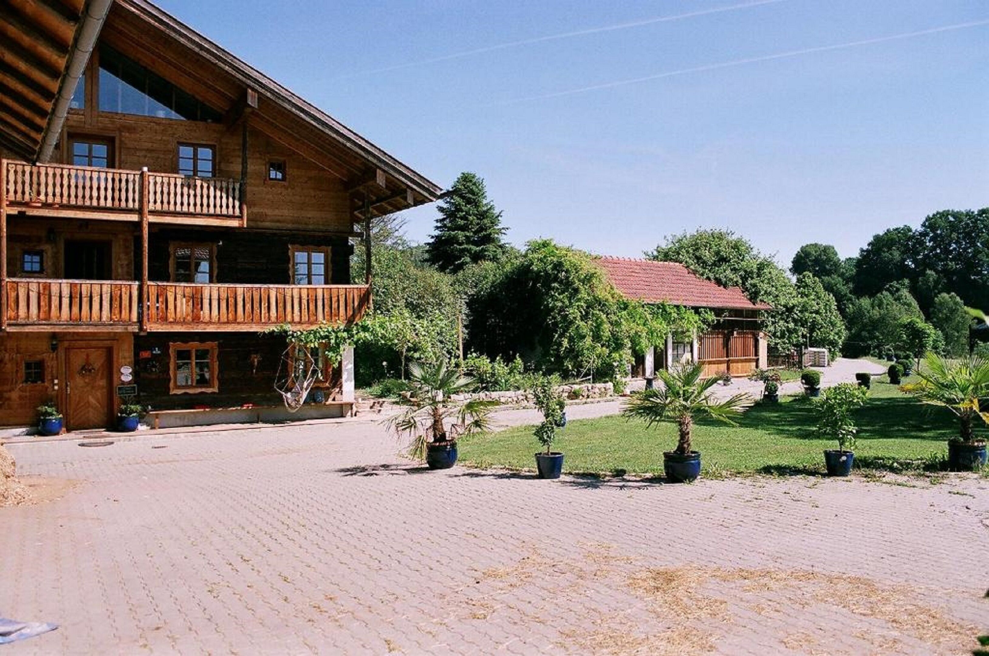 A wooden building with a balcony, surrounded by a paved courtyard and potted plants.