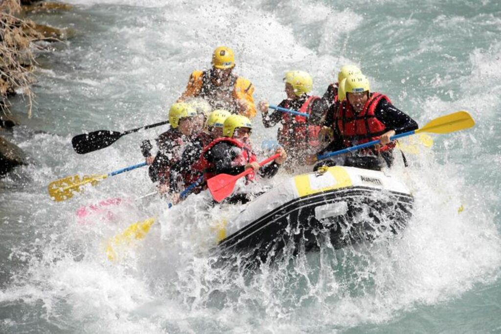 Eine Gruppe von Personen in einem weißen Schlauchboot durchfährt einen reißenden Fluss.