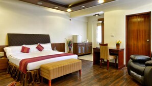 A hotel room with a large bed, a wooden desk, a chair, a small table, and a leather sofa. - Pleasant Boulevard MG Road (Bengaluru)