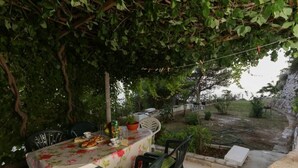 Un espace de restauration en plein air avec une table dressée pour deux personnes, entourée de chaises, sous une voûte de feuillage.