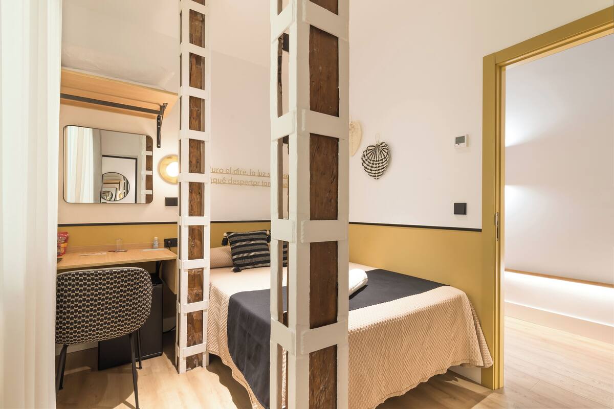 A bedroom with a bed, bedside table, chair, and a mirror.