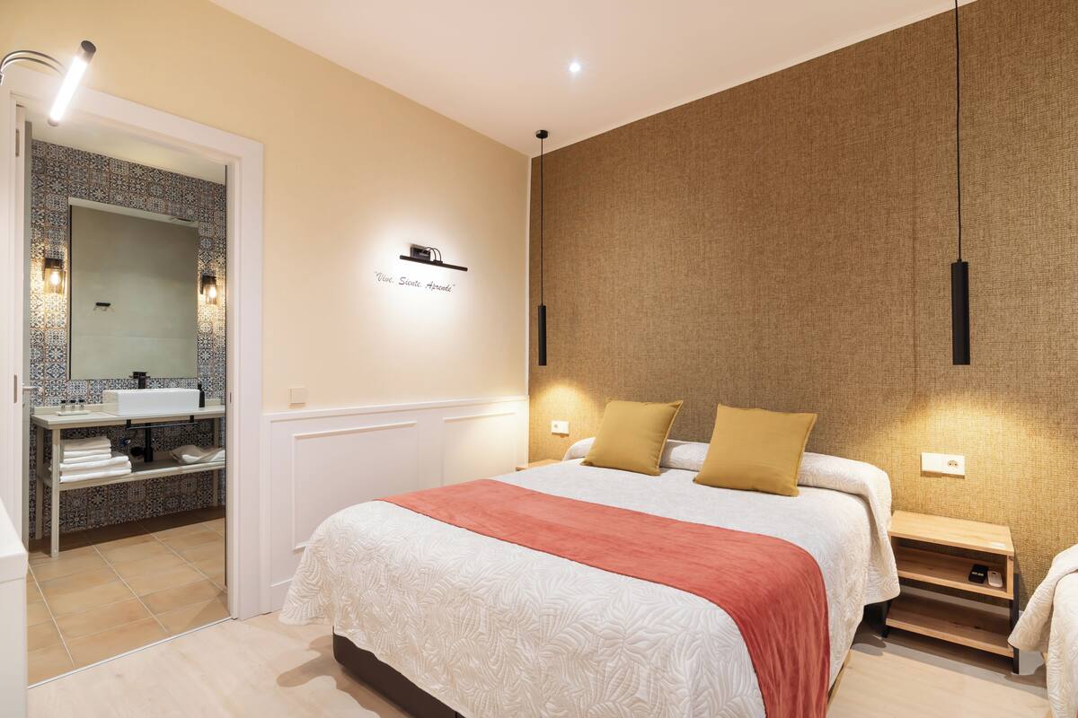 A modern hotel room with a large bed, a bathroom with a mirror and sink, and a textured wall.