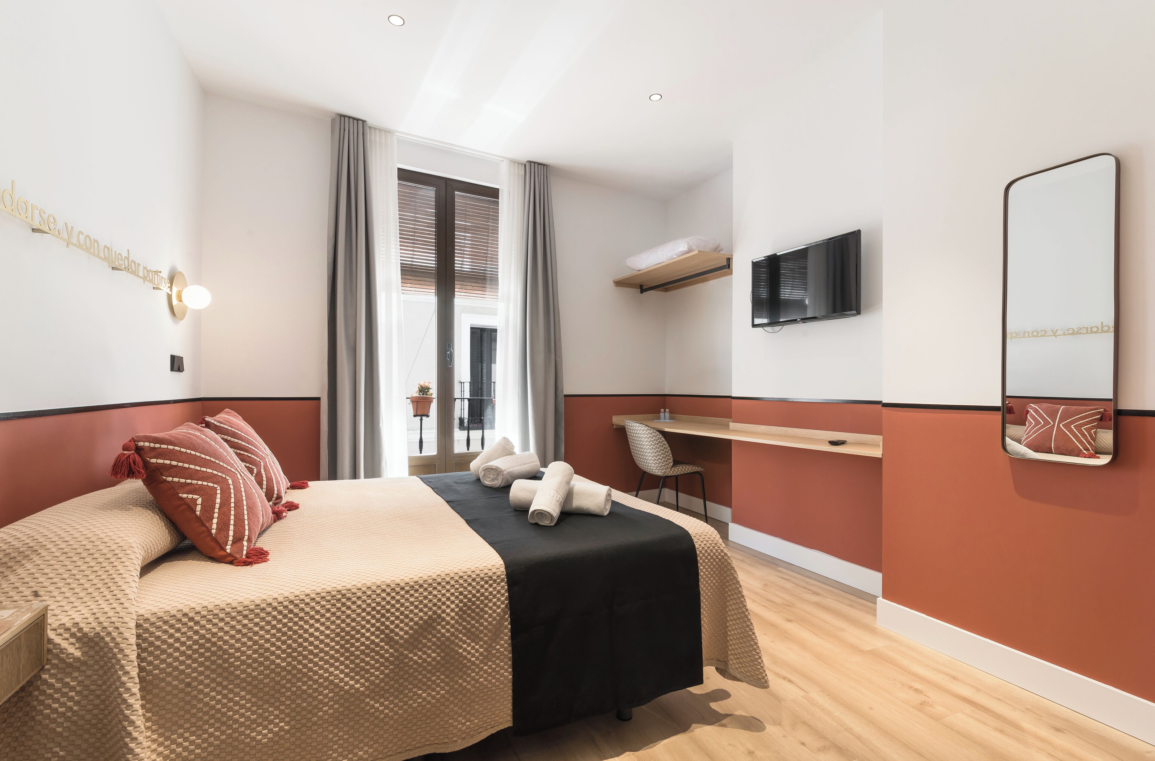 Een moderne hotelkamer met een bed, een bureau, een stoel, een televisie en een grote spiegel.