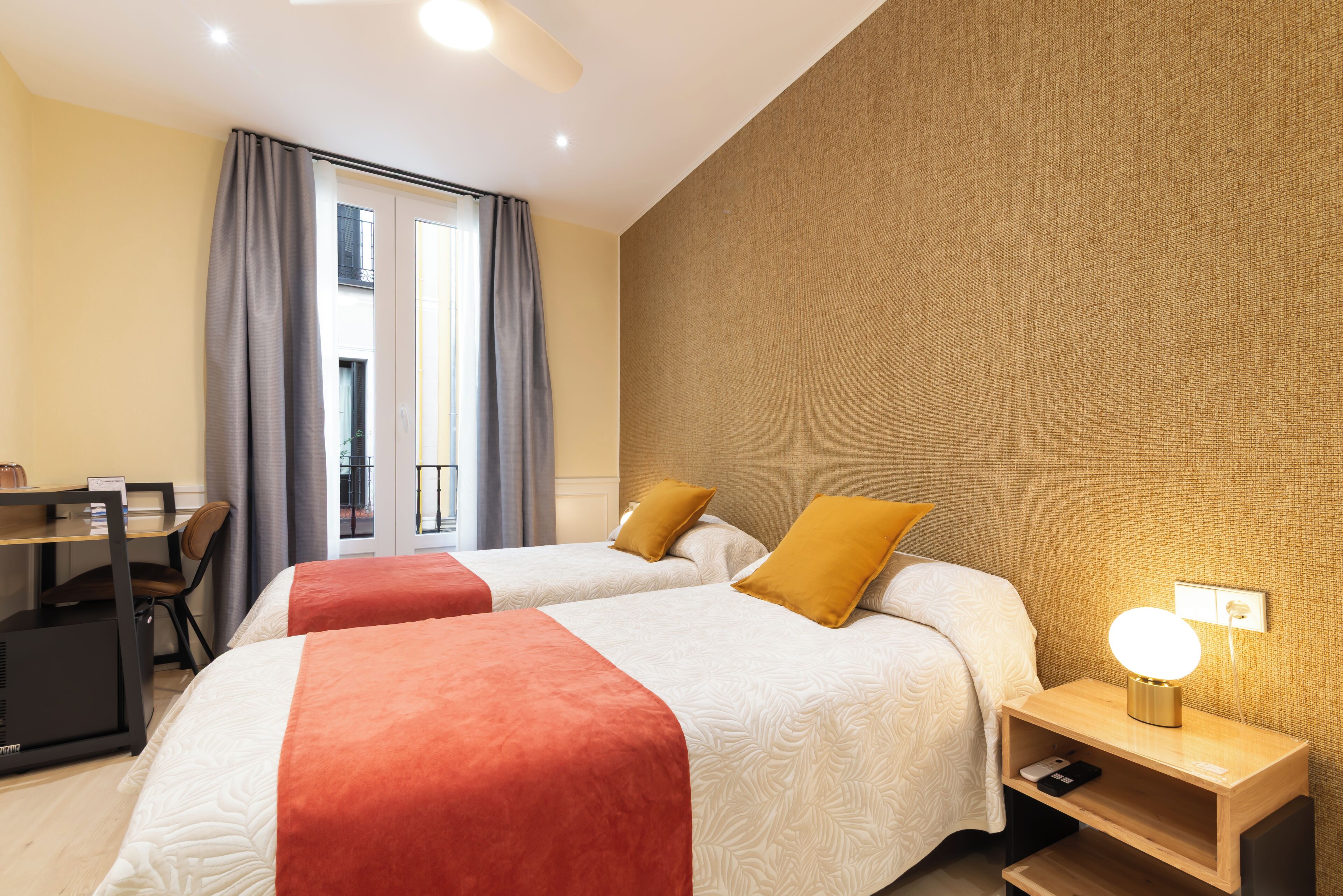 Une chambre d’hôtel avec deux lits, un bureau, une chaise, une table de chevet avec une lampe et une vue sur l’extérieur.