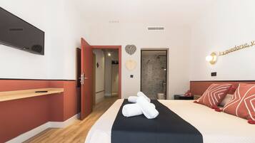 Habitación de hotel con cama, mesita de noche, televisor montado en la pared y puerta que da a un baño.