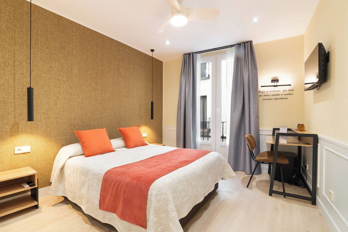A hotel room with a bed, a desk, a chair, a ceiling fan, and a wall-mounted TV.