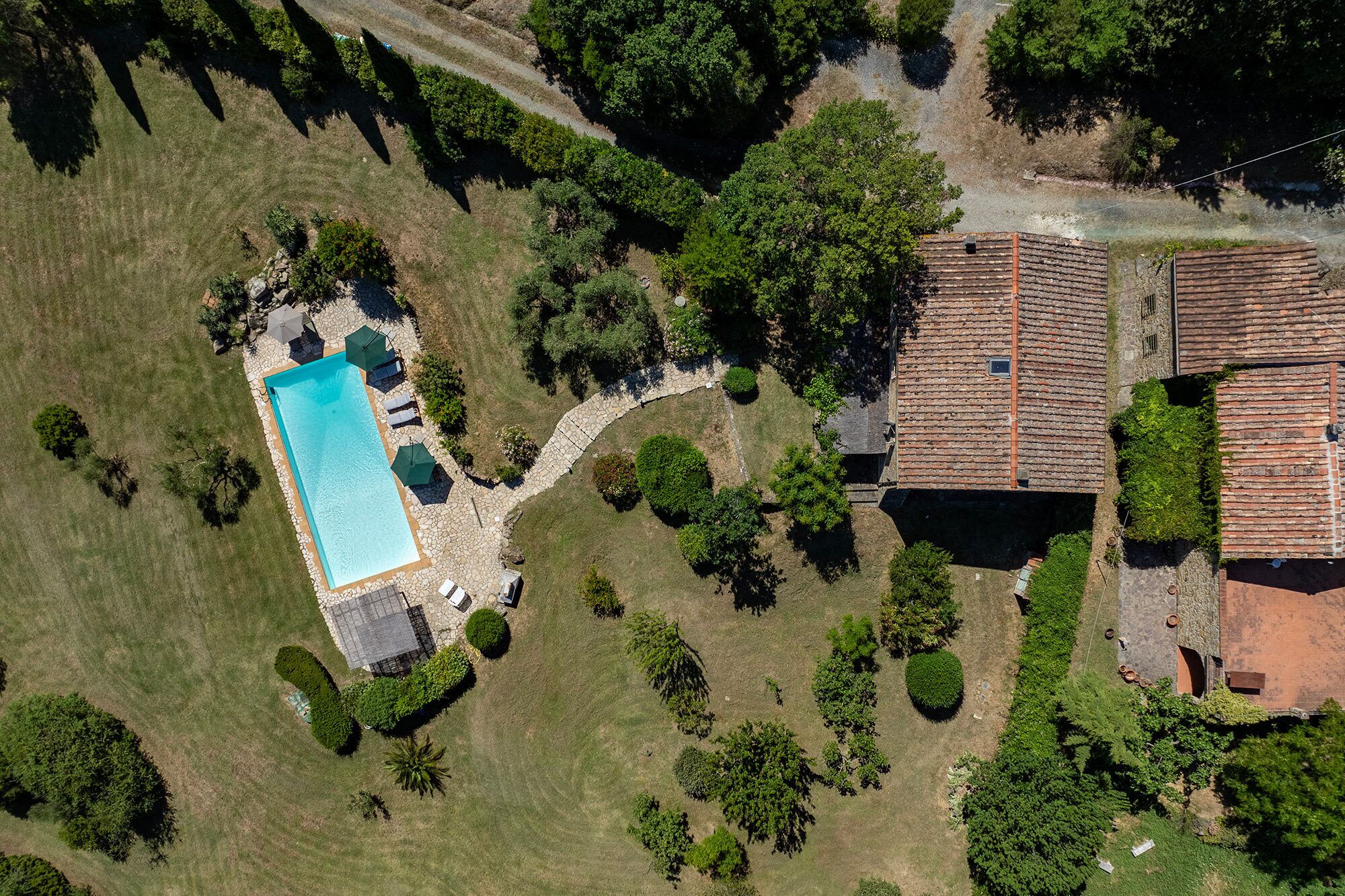 An aerial view of a property with a swimming pool, stone pathway, and surrounding greenery.