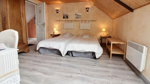 Una camera da letto con soffitto in legno, un letto con biancheria bianca, due comodini con lampade e un termosifone.