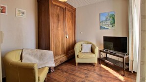 Un soggiorno con un'armadiatura in legno, due poltrone, una TV su un mobile in legno e un quadro appeso al muro.