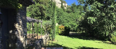 Ein Steinhaus mit überdachter Terrasse, umgeben von üppigem Grün und blauem Himmel.