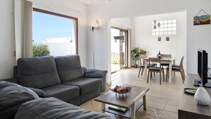 Een woonkamer met een grijze bank, een salontafel en een eethoek met een tafel en stoelen.