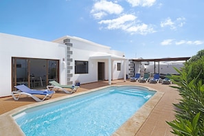 A modern pool area with lounge chairs, a covered seating area, and a building with large windows and a patio.