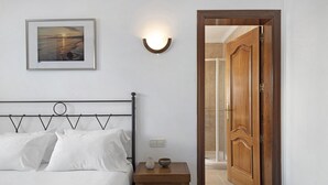 Een slaapkamer met een bed, een nachtkastje met een lamp, een ingelijst beeld aan de muur en een houten deur die naar een badkamer leidt.
