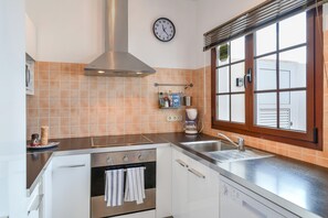 Een keuken met een fornuis, oven, spoelbak en raam met jaloezieën.
