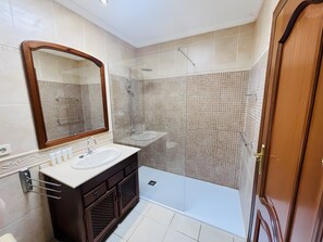 Un baño con un espejo grande, un lavabo, una ducha y una puerta.