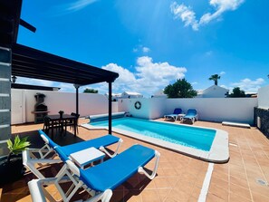 Un área de piscina en la azotea con sillones de descanso, una parrilla y un pérgola.