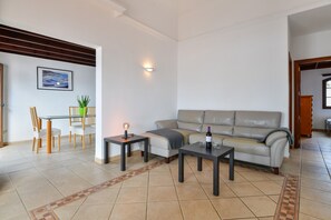 A living room with a sofa, two tables, a dining table with chairs, and a wall-mounted light fixture. - Vacation Home Villa Gauda with Mountain Views, Wi-Fi and Private Pool (Lanzarote)
