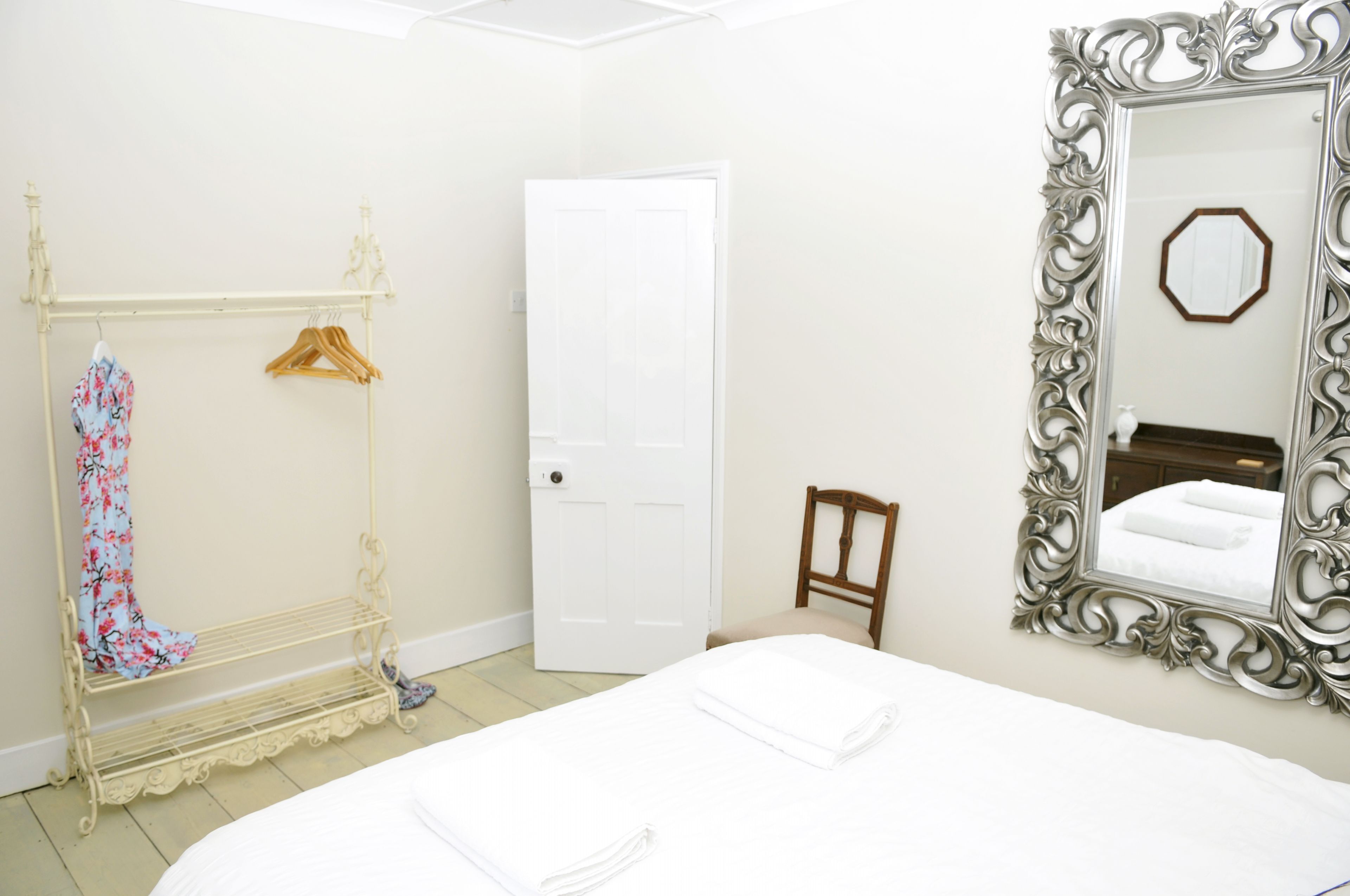 A hotel room with a bed, a wardrobe with hangers, a door, and a mirror with an ornate frame.