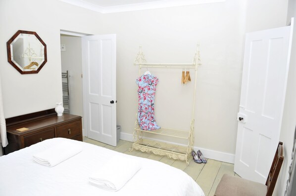 A hotel room with a bed, a wooden dresser, a mirror, a clothing rack, and a door.