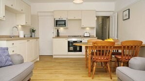 A compact kitchen with white cabinets, a built-in oven, and a dining area with wooden chairs and a table. - Little Lane is a charming, recently refurbished 2 bedroom cottage sleeping 4 (Gosport)