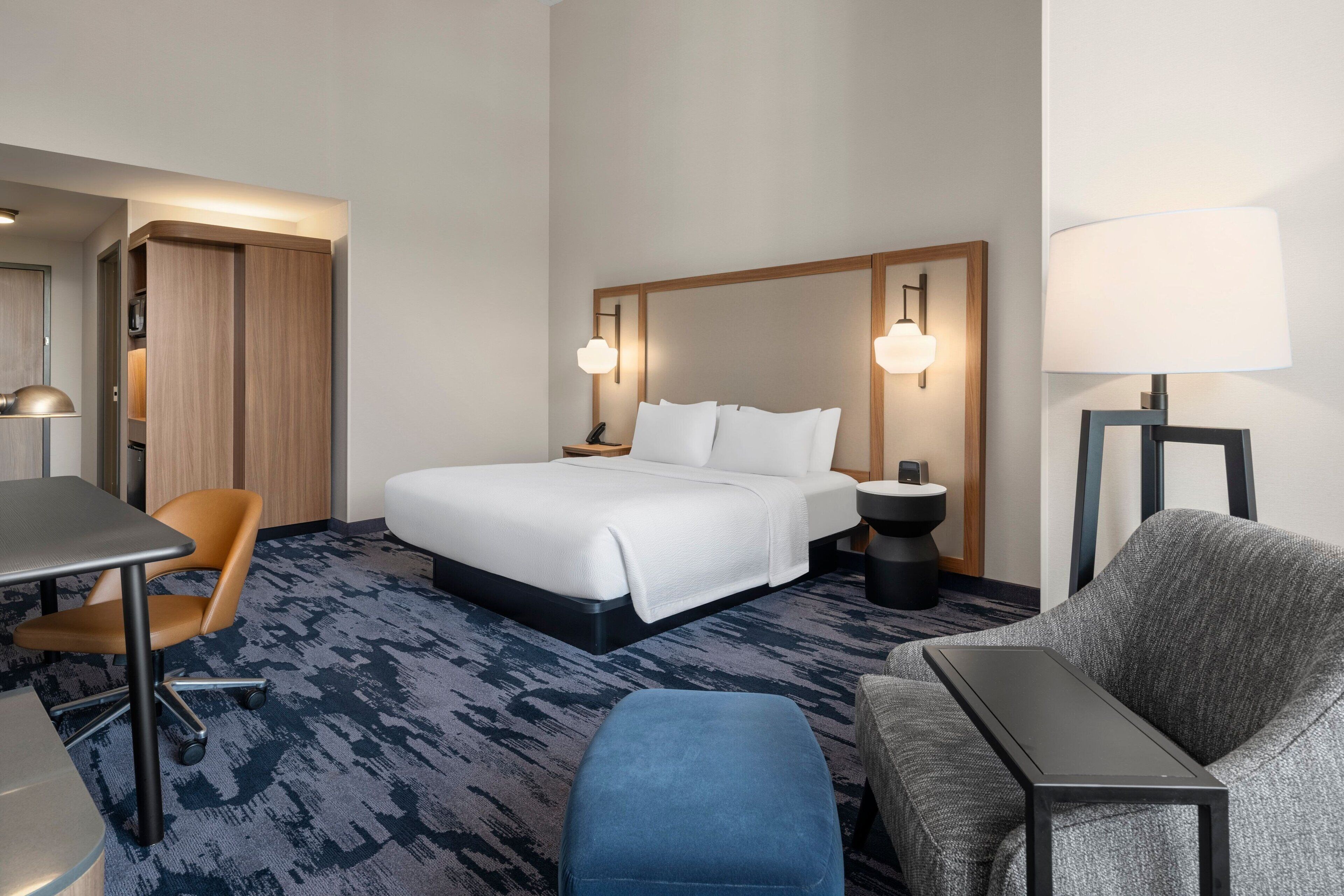 A hotel room with a bed, a desk, a chair, a sofa, and a lamp.