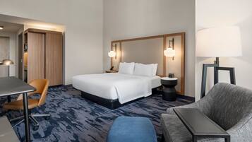 A hotel room with a bed, a desk, a chair, a sofa, and a lamp.