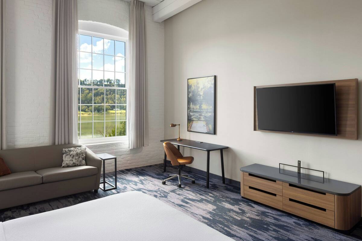 Une chambre d’hôtel avec un grand lit, un bureau avec une chaise, une télévision et une fenêtre avec des rideaux.