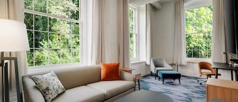 Una habitación de hotel moderna con un ventanal grande, un sofá, una mesa de centro y un escritorio.