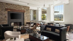 A spacious living area with a stone wall, modern furniture, and large windows offering a view of the outdoors. - Fairfield Inn & Suites Madison Historic Eagle Cotton Mill (Madison)
