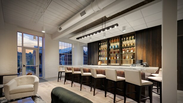 A modern bar area with a long counter, multiple stools, and a well-stocked liquor display. - Fairfield Inn & Suites Madison Historic Eagle Cotton Mill (Madison)