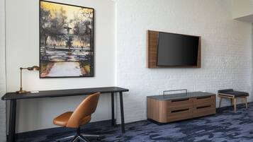 Una habitación moderna con escritorio, silla, televisor y obra de arte en una pared de ladrillo blanco.
