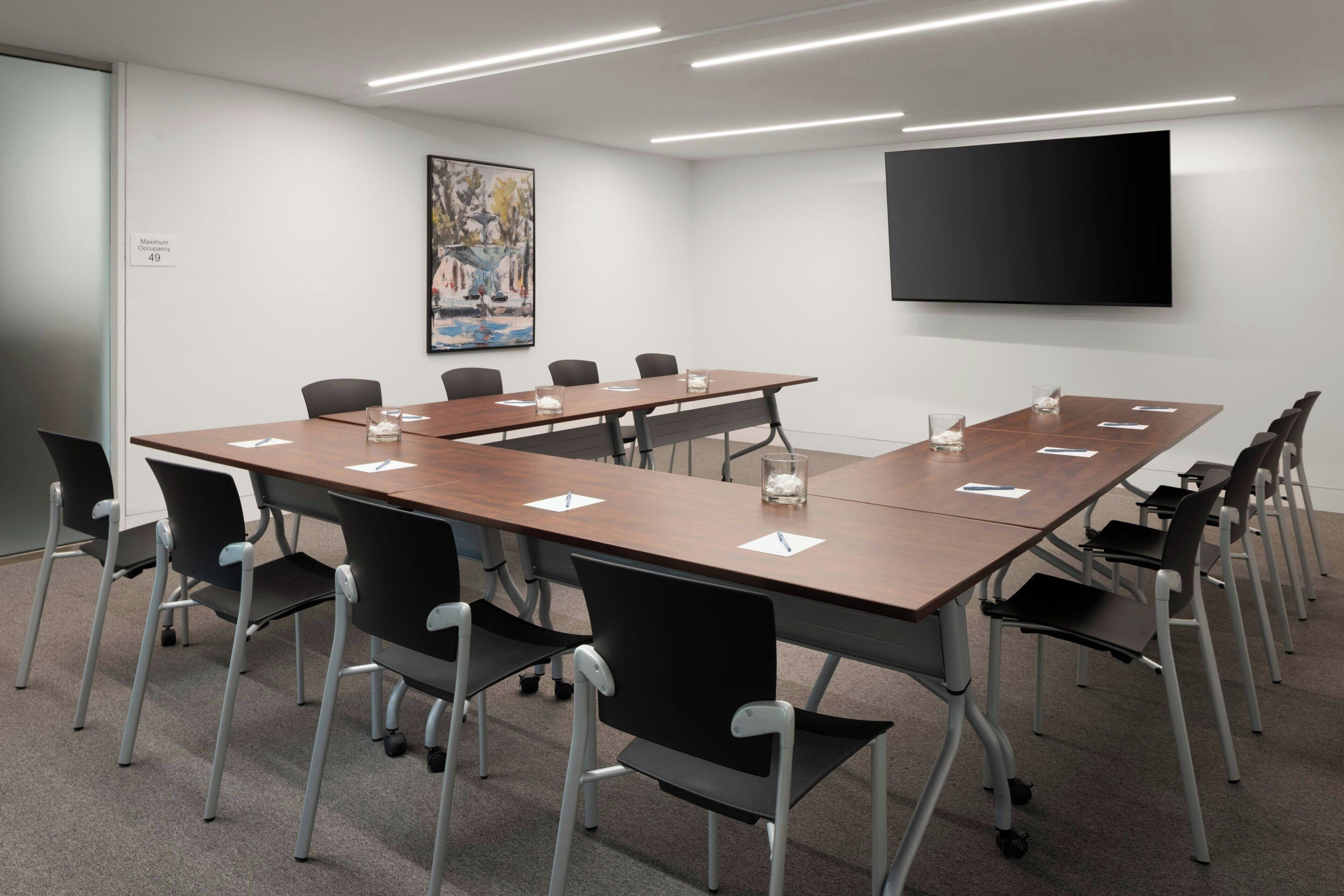 A conference room with a long table, black chairs, a flat-screen TV, and a painting on the wall.