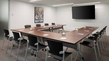 A conference room with a long table, black chairs, a flat-screen TV, and a painting on the wall.