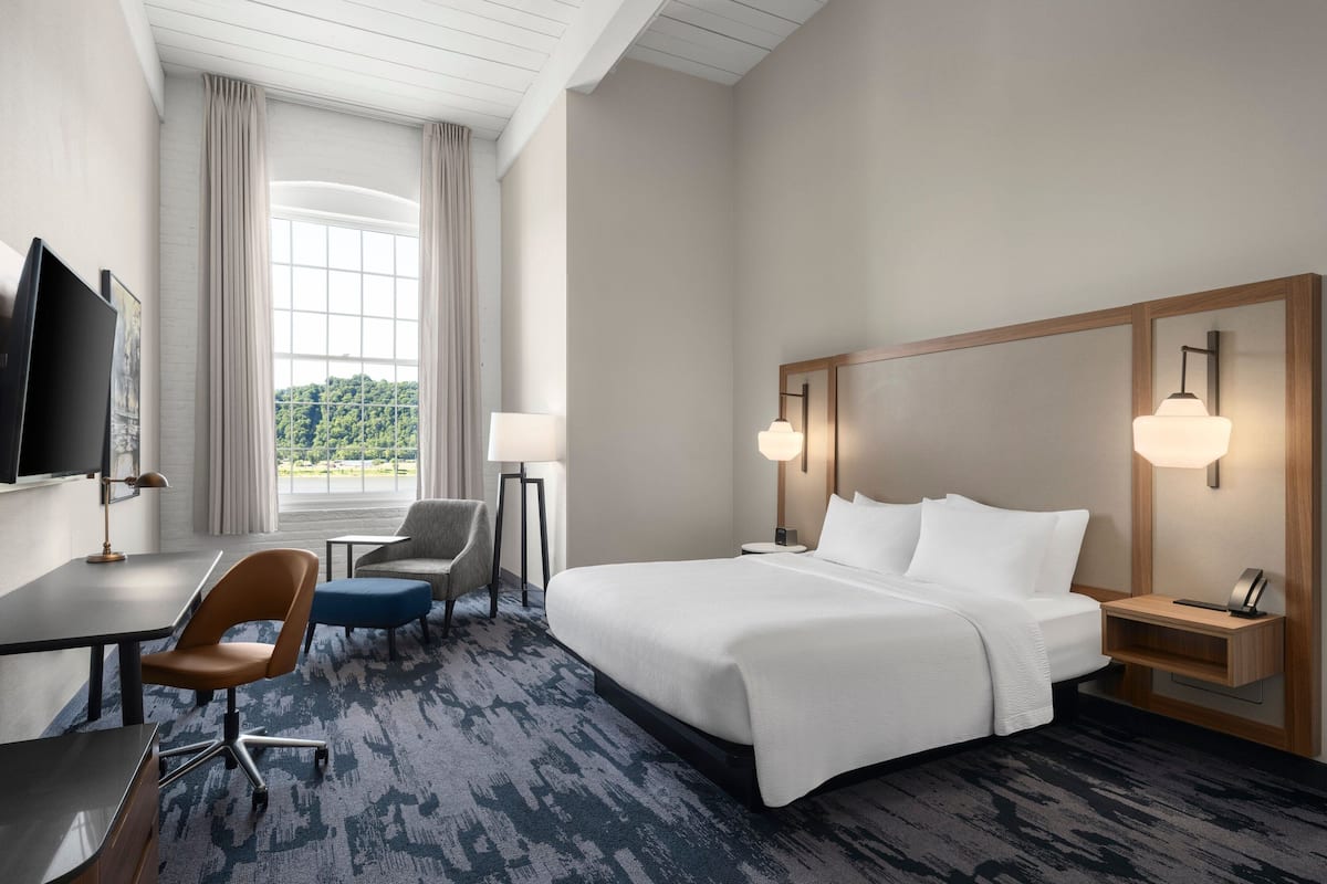 Une chambre d’hôtel avec un grand lit, un bureau, une chaise, une télévision et une fenêtre avec des rideaux.