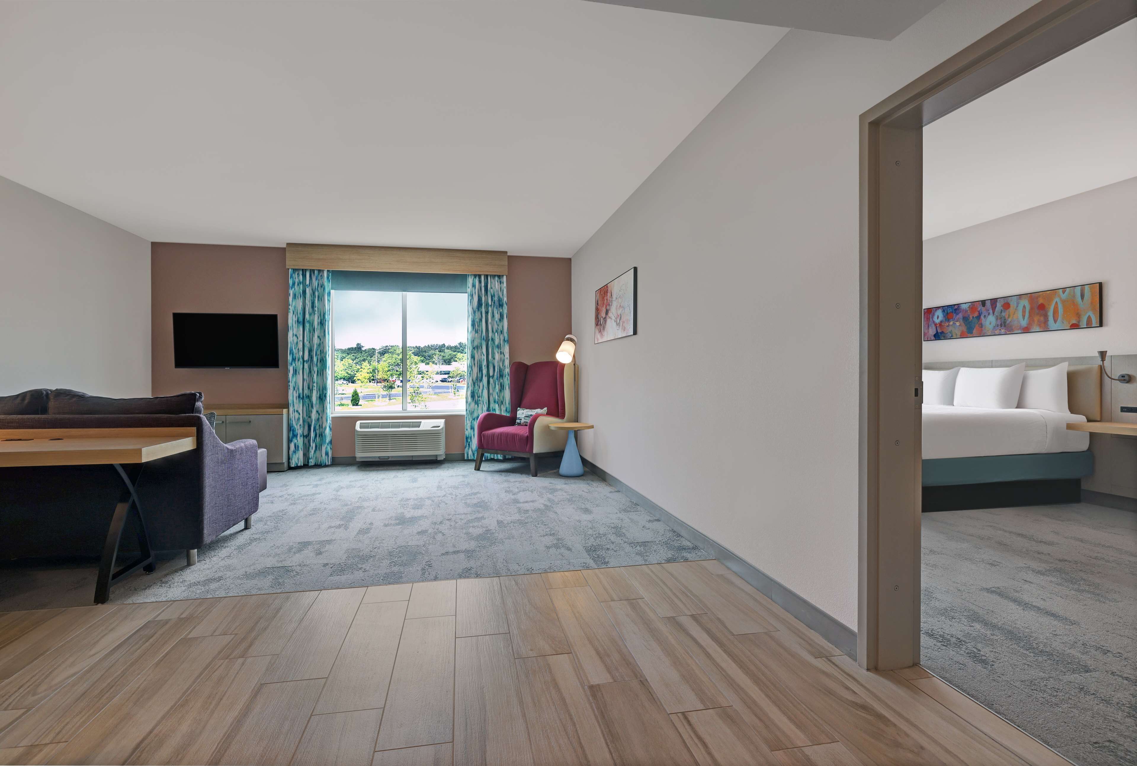 A hotel room with a bed, a desk, a chair, a TV, and a window with curtains.