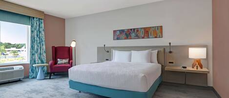 Ein Hotelzimmer mit einem großen Bett, einem roten Sessel, einem kleinen runden Tisch und einem Nachttisch mit Lampe.